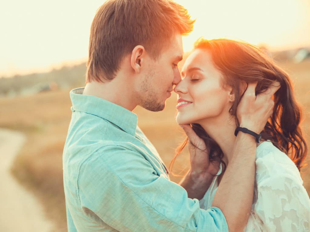 A man and woman kissing in a field at sunset.