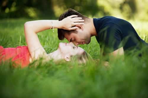 A man and woman kissing in the grass.