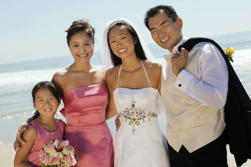 A group of brides and grooms posing for a photo on the beach.