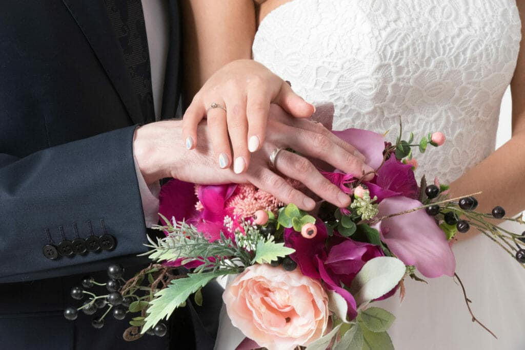 A bride and groom holding hands with a bouquet of flowers.