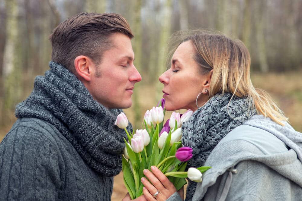 A man and woman kissing while holding a bouquet of tulips.