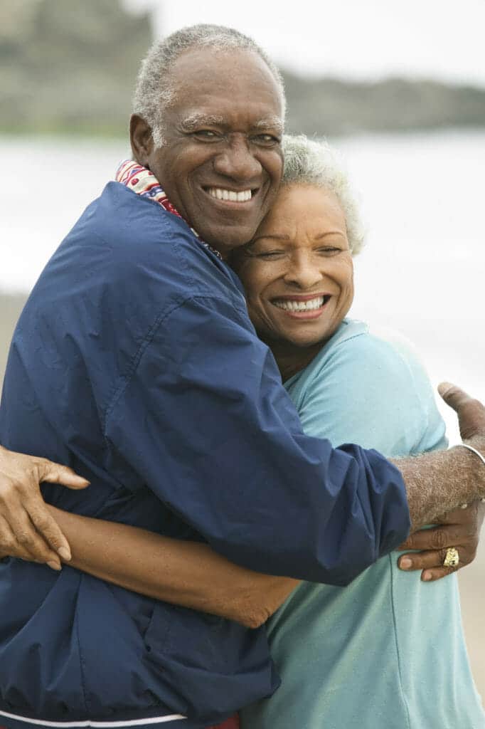 An older couple hugging on the beach.