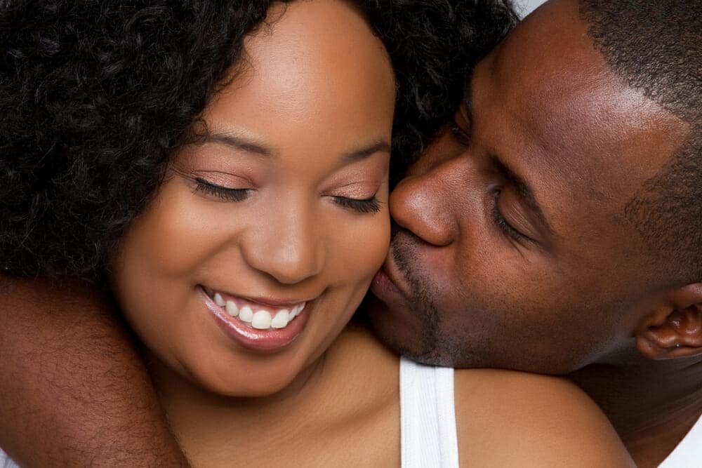 A black man and woman kissing on the cheek.