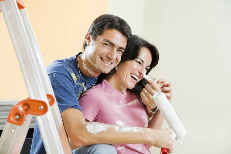 A man and woman smiling while painting a room.