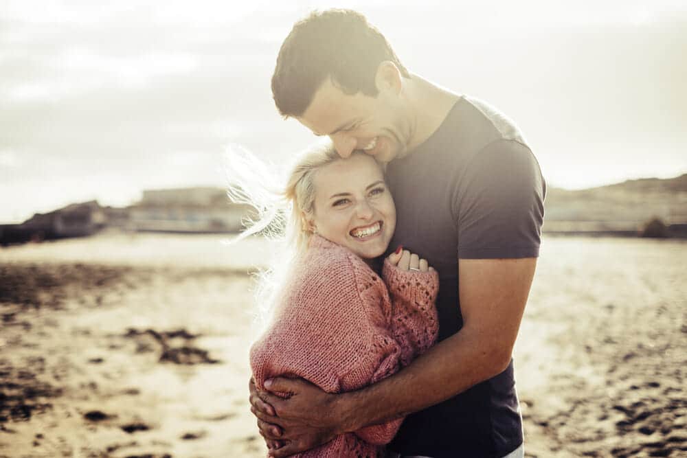 A man and woman hugging on the beach.