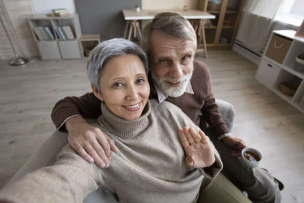 An older couple taking a selfie in their living room.