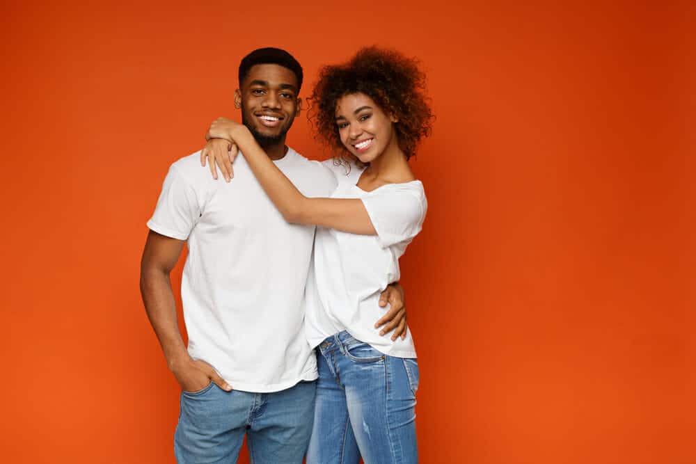 A young black couple posing against an orange background.