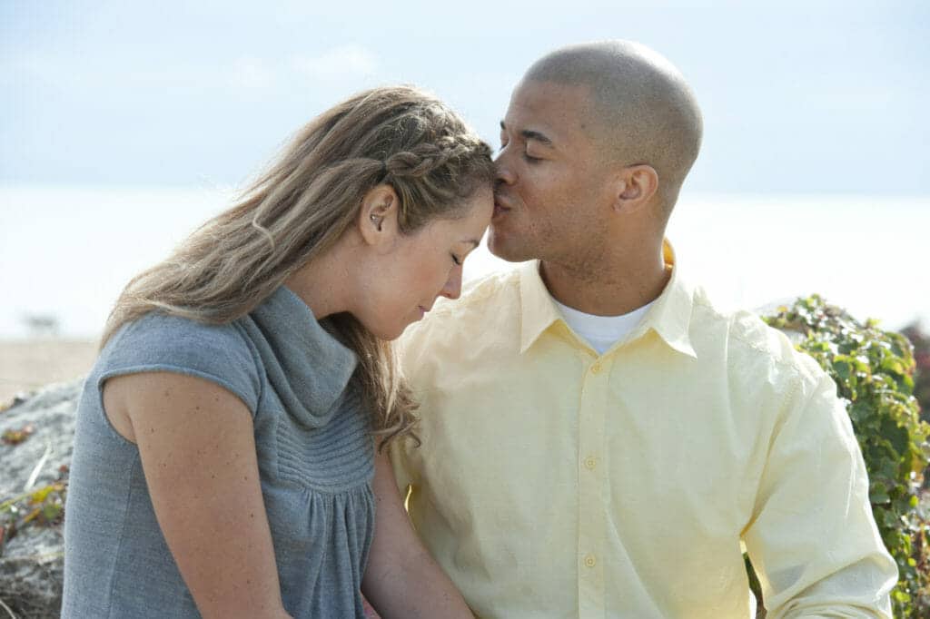 A man and woman kissing on the beach.