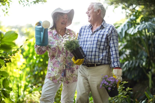 An older couple holding gardening tools in a garden.