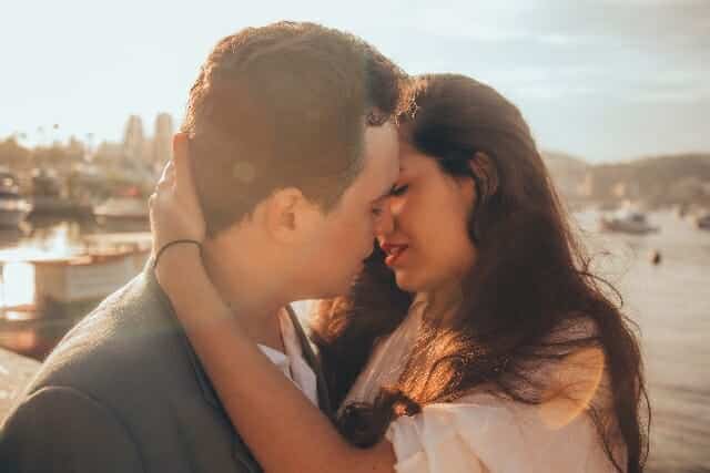 A man and woman embracing in front of the water.