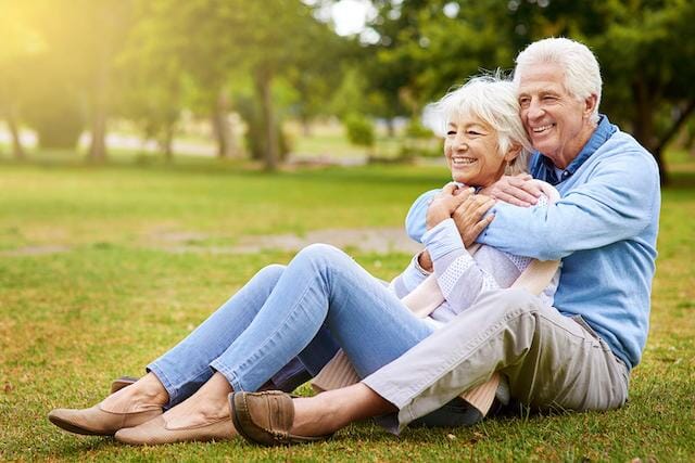 An older couple sitting on the grass in a park.