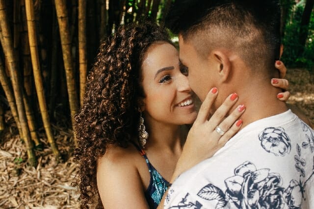 A man and woman hugging in front of bamboo trees.