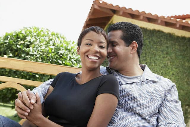 A man and woman sitting on a bench in front of a house.