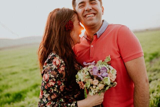 A man and woman hugging in a field at sunset.