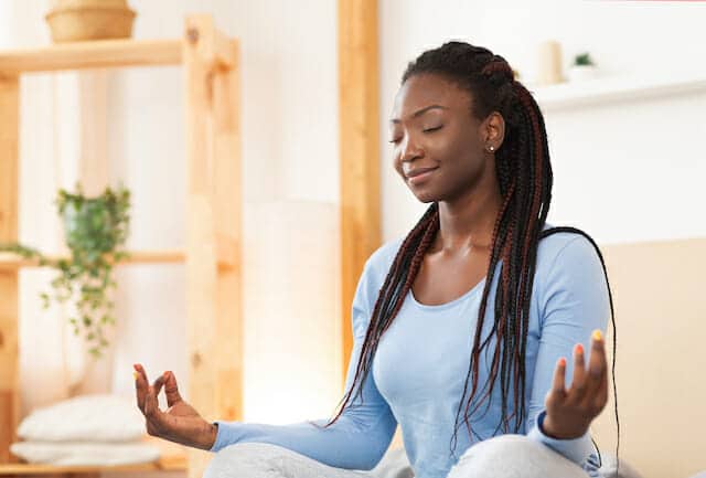 A woman meditating on a bed at home.