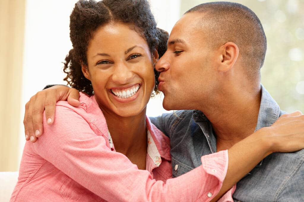 A man and woman kissing while sitting on a couch.