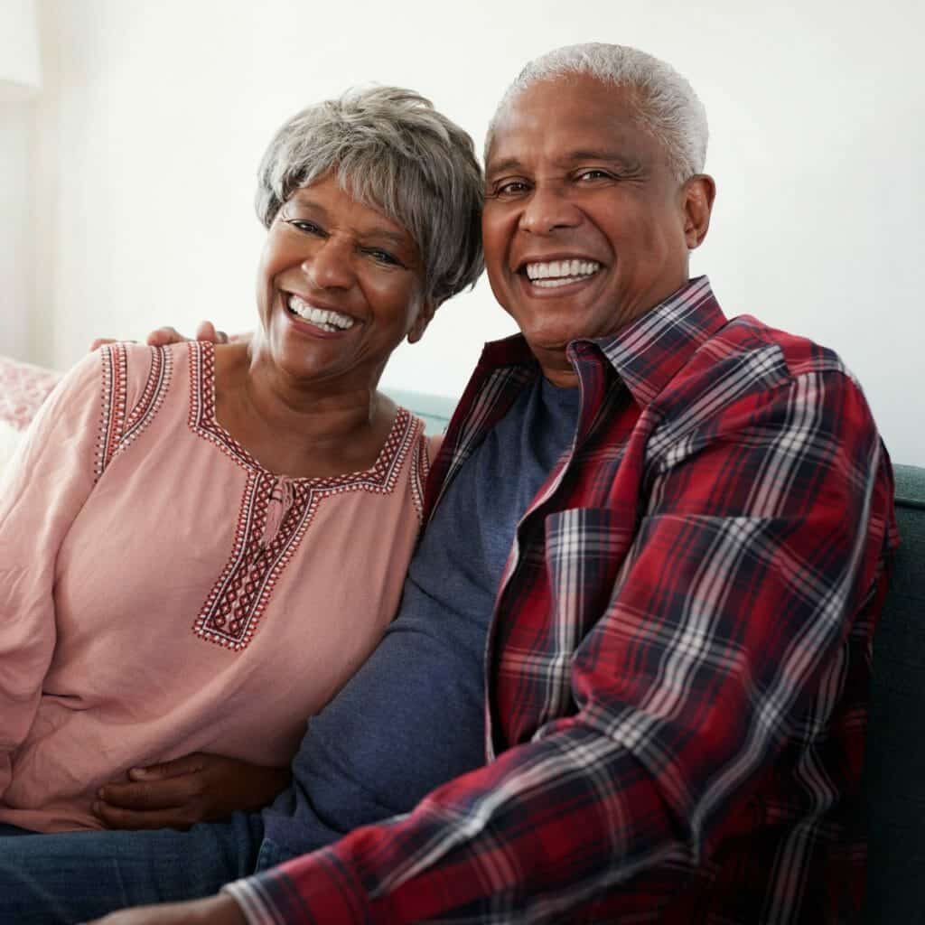 An older couple smiling while sitting on a couch.