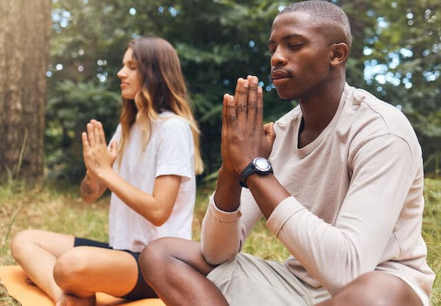 A man and woman doing yoga in the woods.