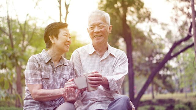 An asian couple sitting on a bench in a park.