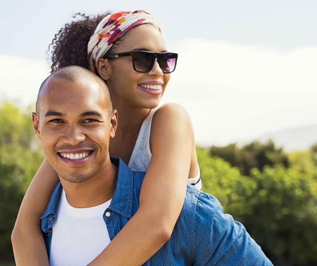 A young black man is carrying a woman on his shoulders.