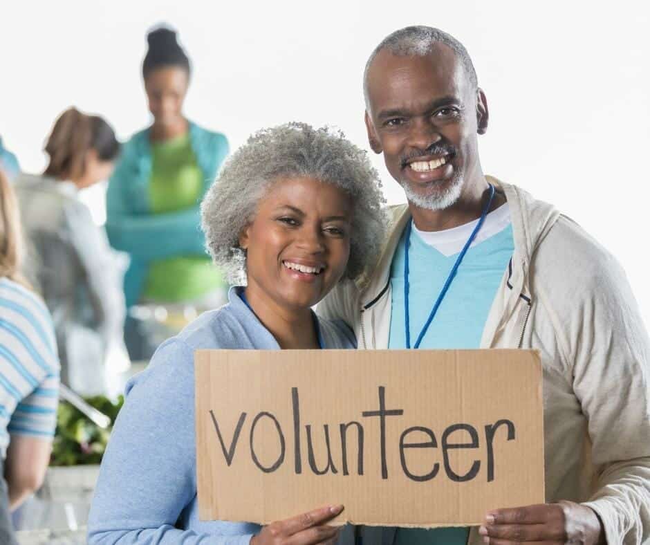 A couple holding up a sign that says volunteer.