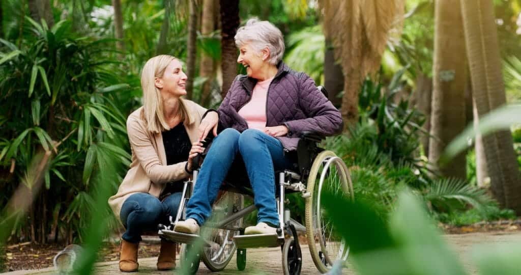 A woman in a wheelchair talking to an older woman in a park.