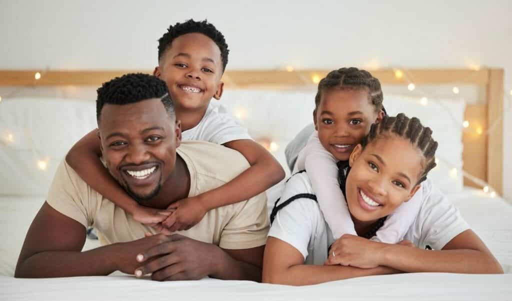 A black family laying on a bed with their children.