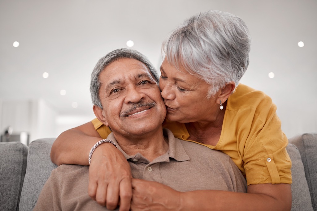 An older couple kissing on the couch.