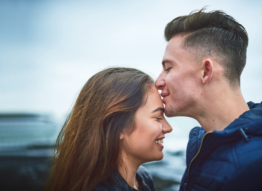 A man and woman kissing each other in front of a cloudy sky.