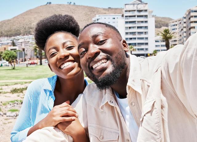 A black man and woman taking a selfie in front of a city.