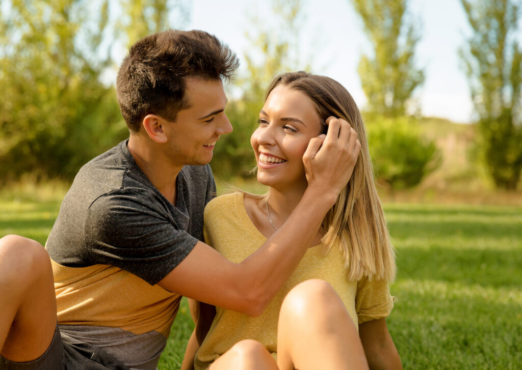 A young man and woman are sitting on the grass together.