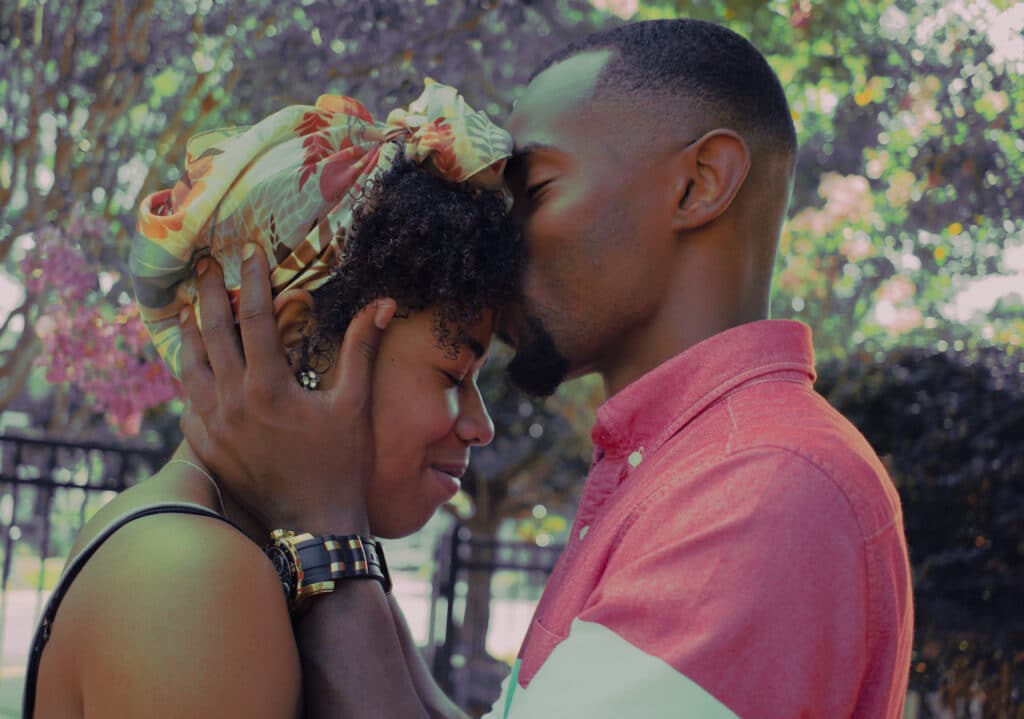 A man and woman kissing in front of a tree.