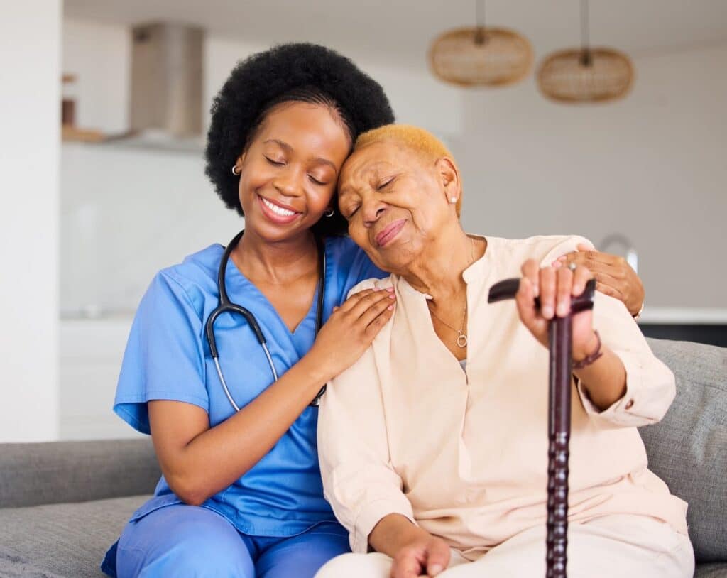 A nurse is hugging an elderly woman on the couch.